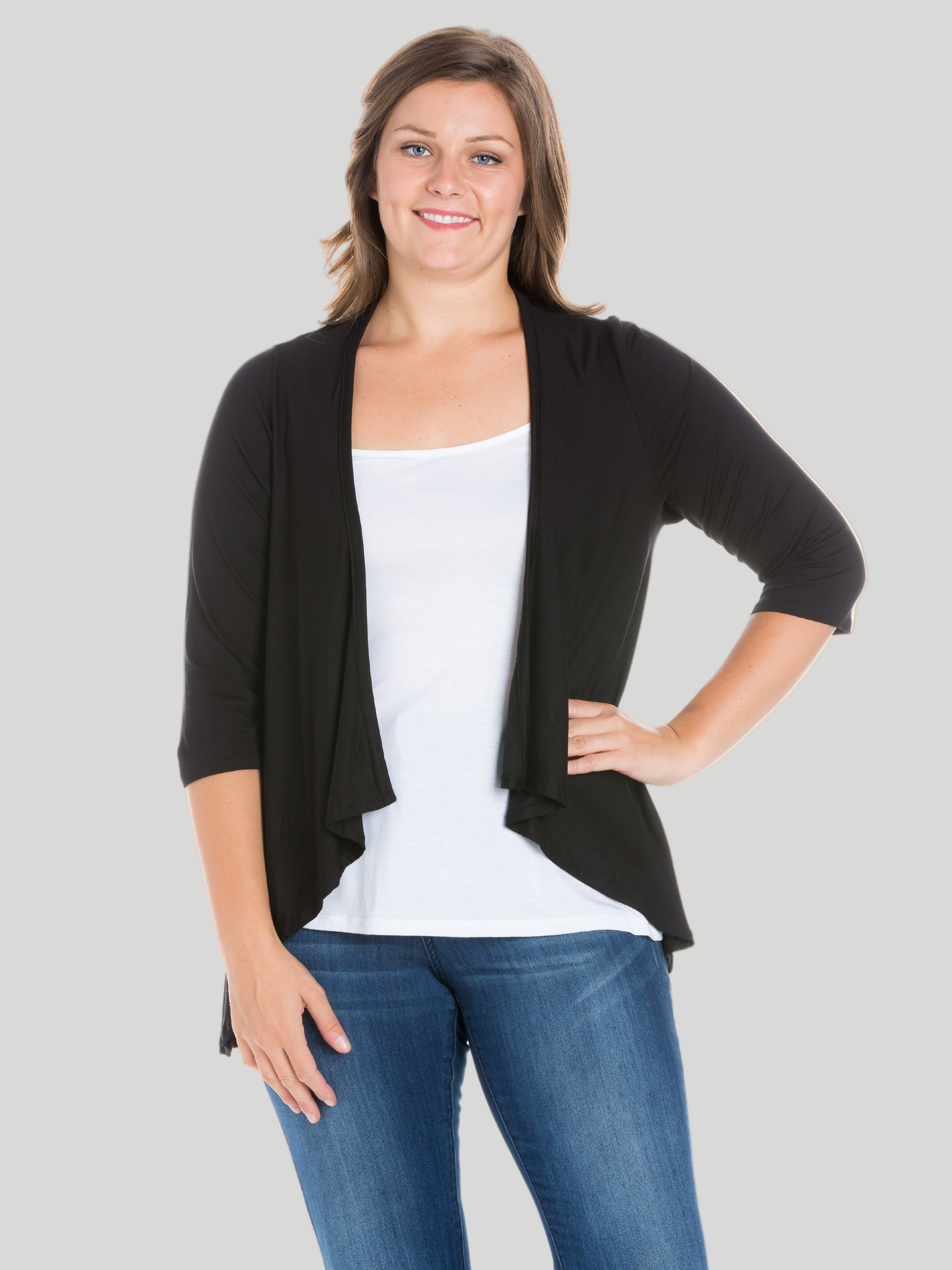 A plus size model wearing an open front black cardigan with elbow length sleeves over a white top and blue jeans.