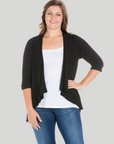 A plus size model wearing an open front black cardigan with elbow length sleeves over a white top and blue jeans.